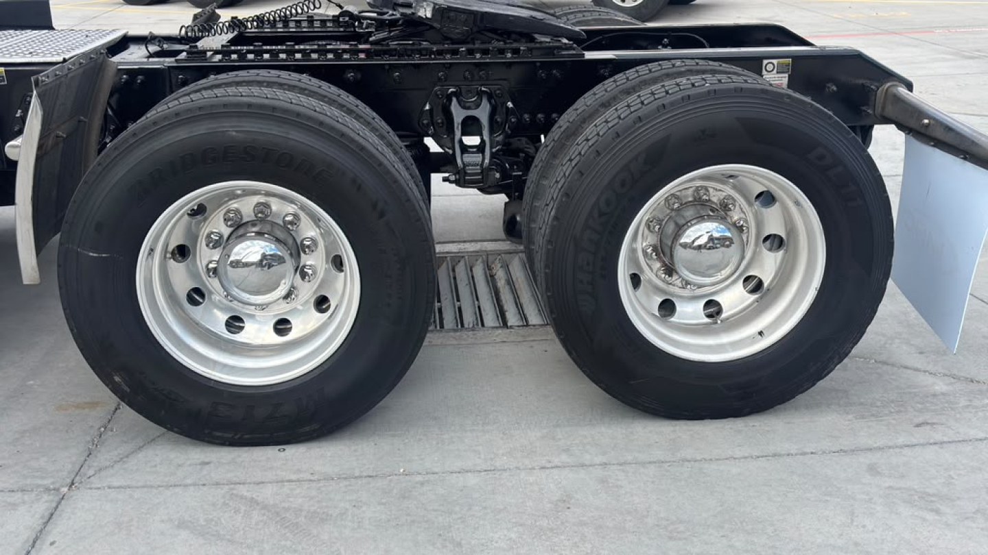 Kenworth T680 axle area showing dual rear wheels and tires with chrome hubcaps, undercarriage and frame in view.