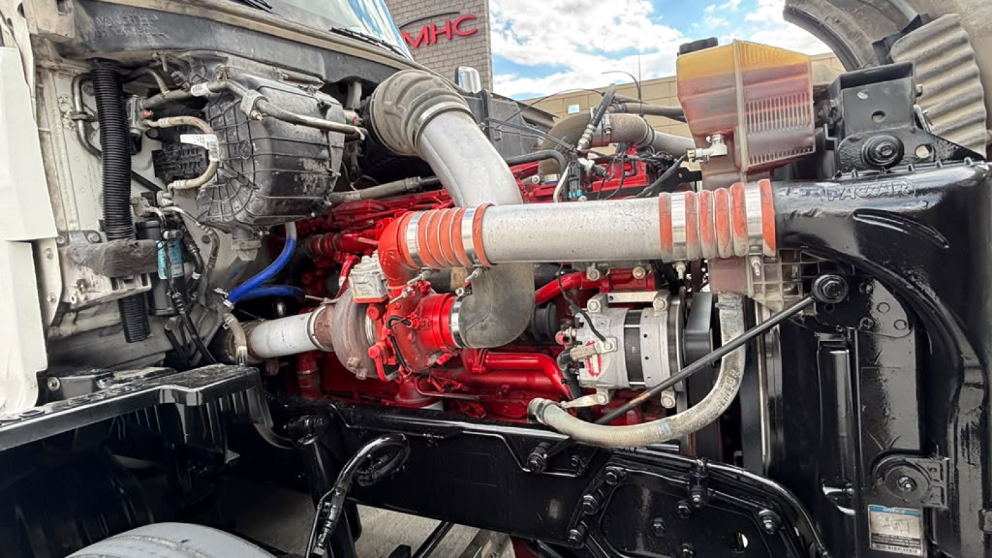 Kenworth T680 engine bay showing red engine block, intake piping, coolant reservoir, and surrounding components.