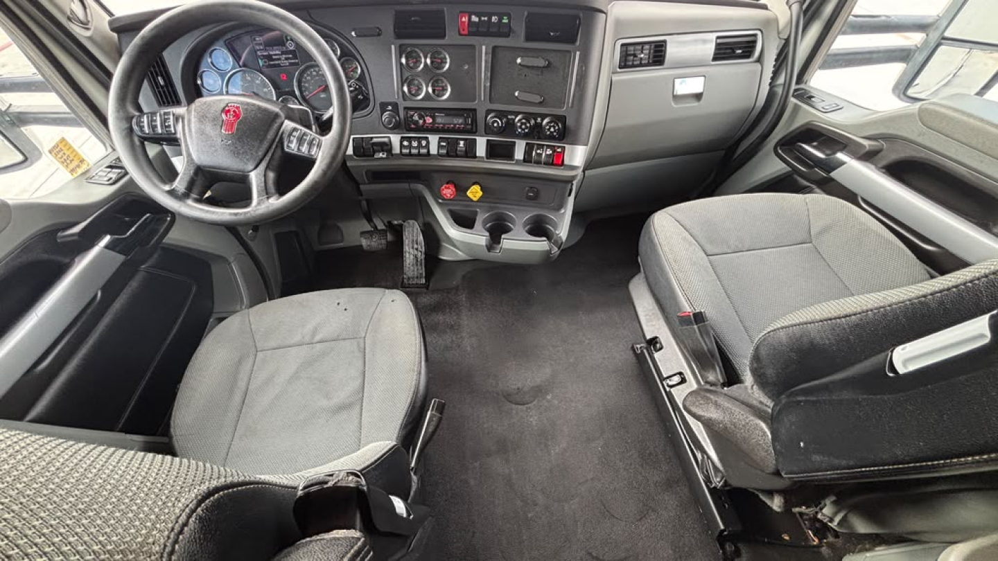 Interior of a 2022 Kenworth T680 cab showing steering wheel, dashboard, driver seat, and passenger seat with central controls.