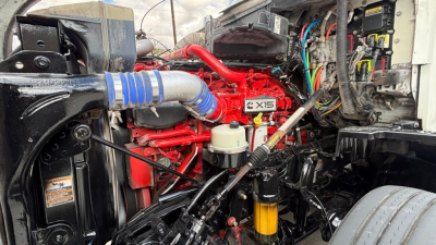 Kenworth truck engine bay with red engine labeled X15 and various hoses and wiring visible.