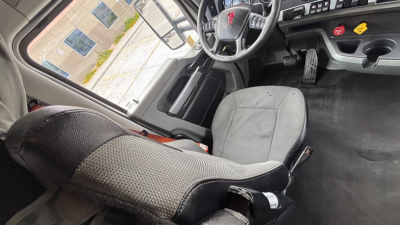 Interior cabin of a 2022 Kenworth T680 showing driver seat and dashboard with steering wheel and pedals; visible wear-free upholstery and controls.