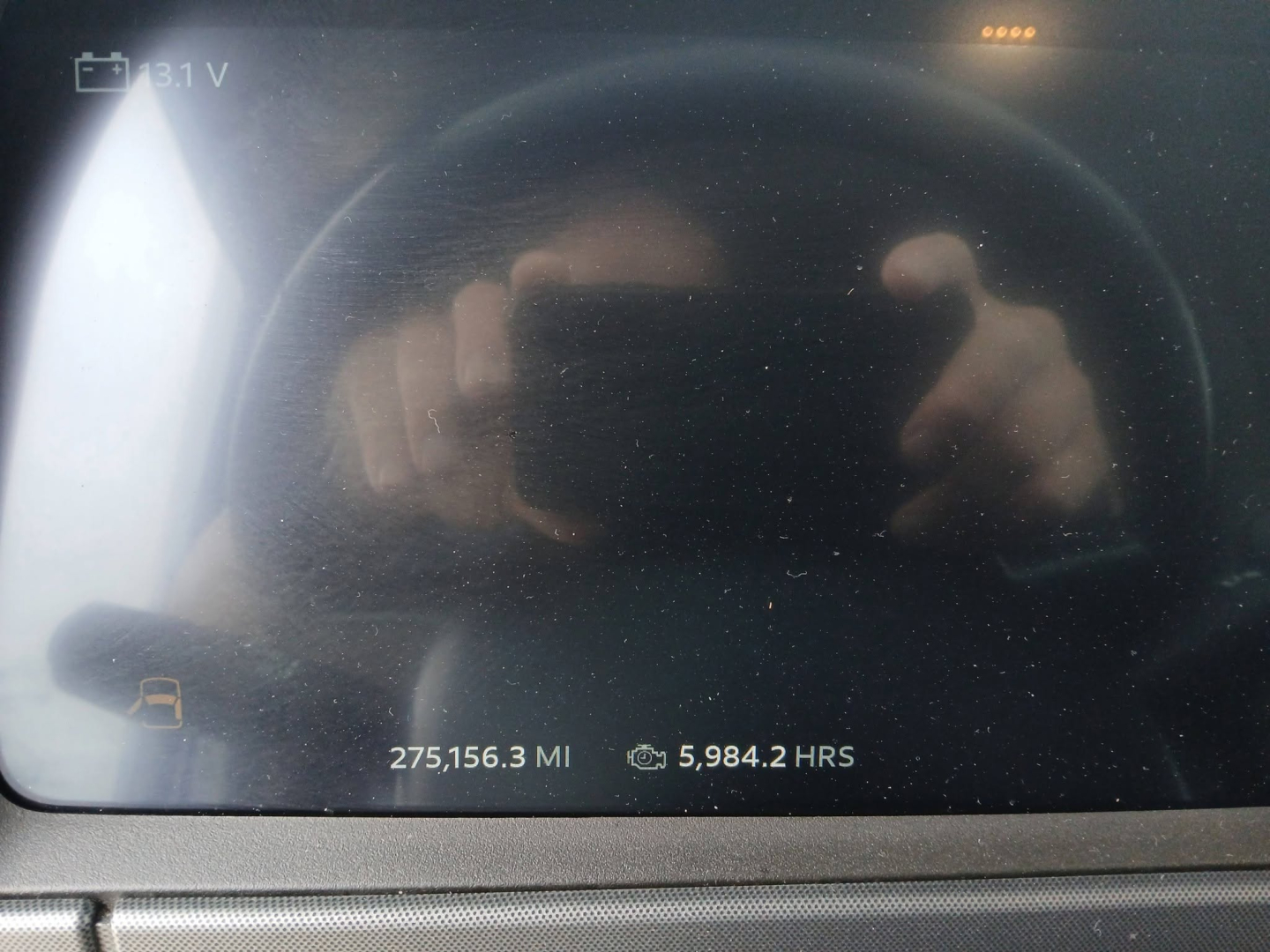 Vehicle dashboard display showing mileage 275,156.3 MI and hours 5,984.2 HRS with a reflection of a person taking a photo.