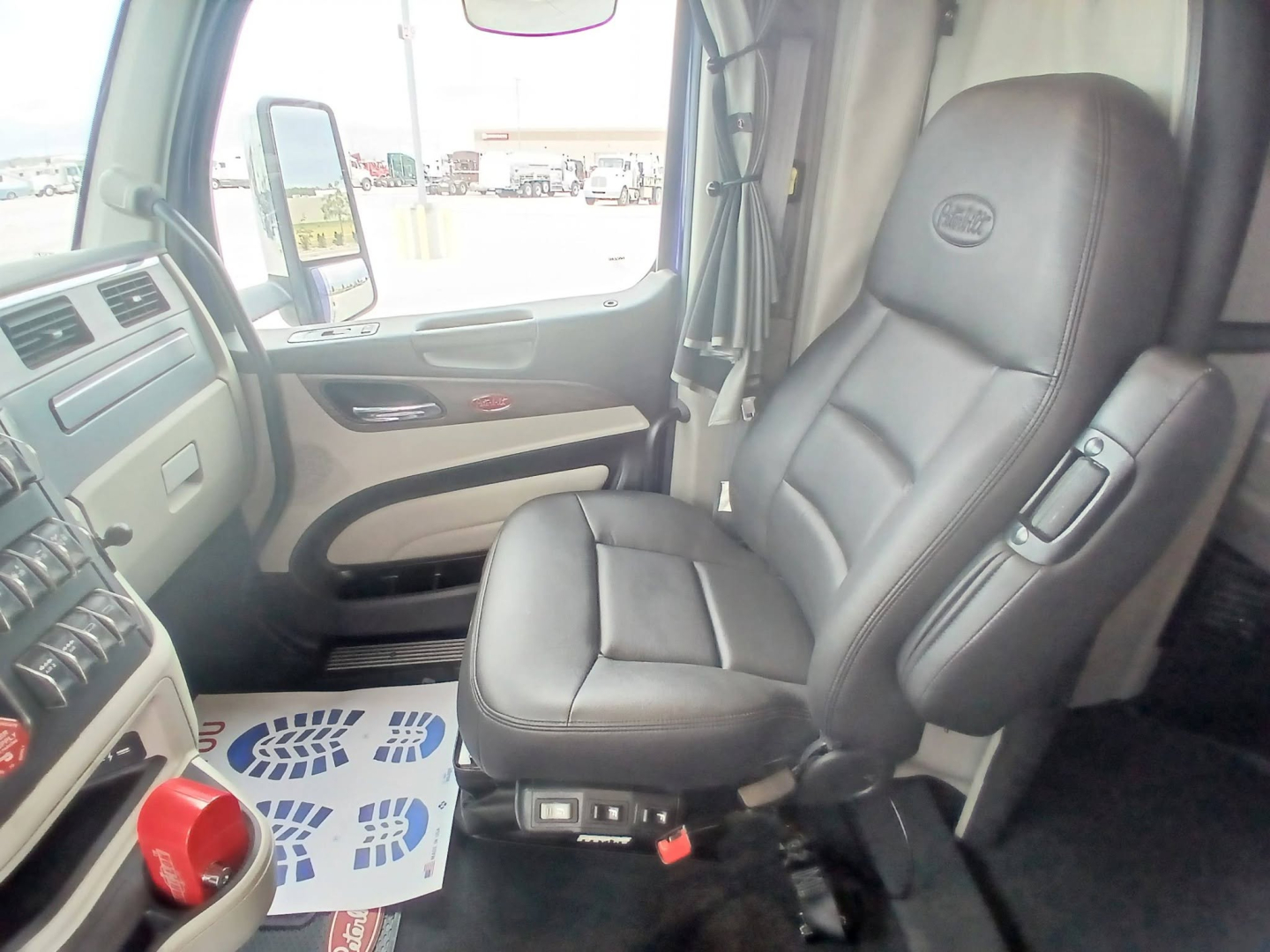 Truck interior seat and dashboard of a Peterbilt 579 cab with driver seat visible, steering wheel area, window, and controls.