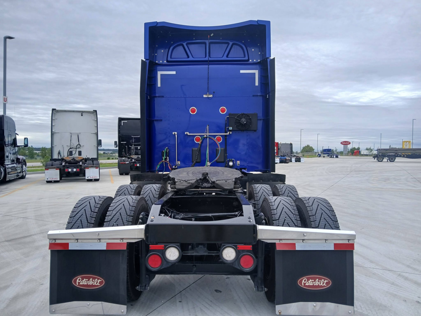 Peterbilt 579 conventional sleeper truck rear view showing fifth wheel, dual rear axles, taillights, mud flaps with Peterbilt logos, and chassis frame.