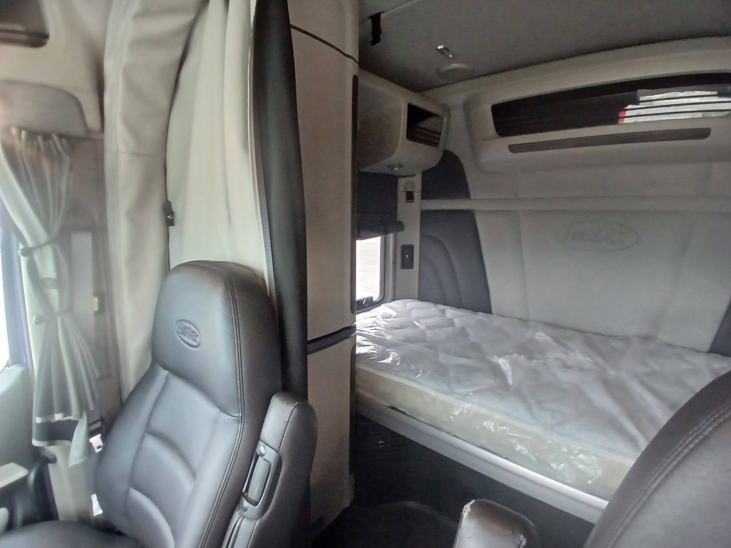 Peterbilt truck sleeper cab interior with bunk bed, control panel, and seat in foreground.