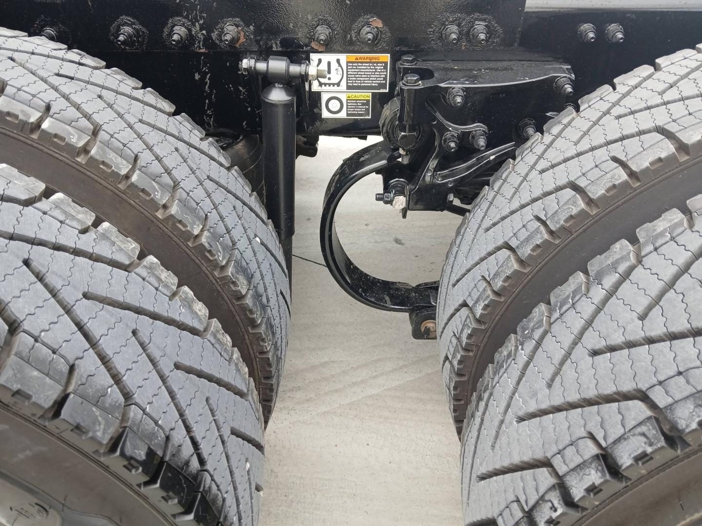 Peterbilt 579 truck dual rear tires with chassis and suspension components visible between wheels; warning sticker and hydraulic lines near the frame.
