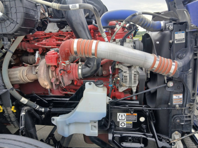 Peterbilt 579 truck engine bay with red engine components, white coolant reservoir, and orange intake hose.