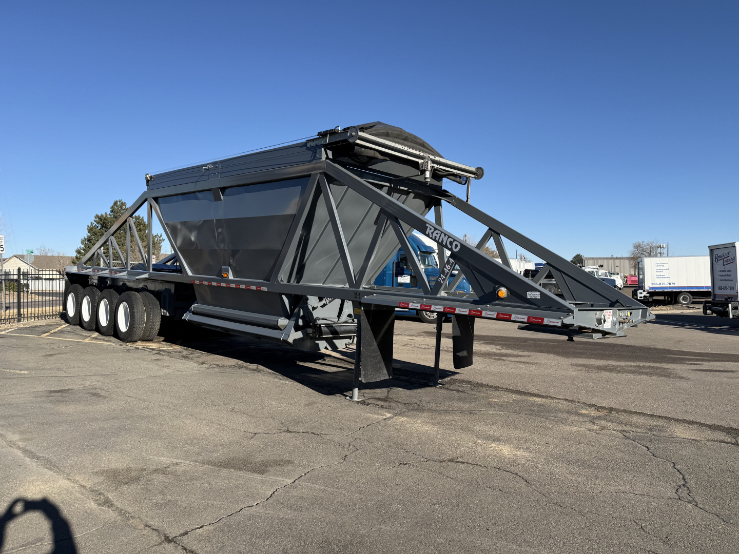Dump trailer showing large steel frame with triangular side rails and multi-axle wheels, 2026 Ranco LW24464 model, parked on lot.