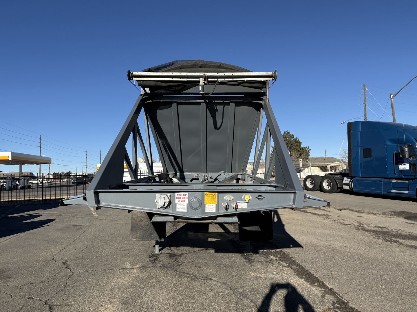 Dump trailer in view showing LW24464 model with hopper and frame structure, front view with metal supports and warning labels, blue semi-trailer in background.