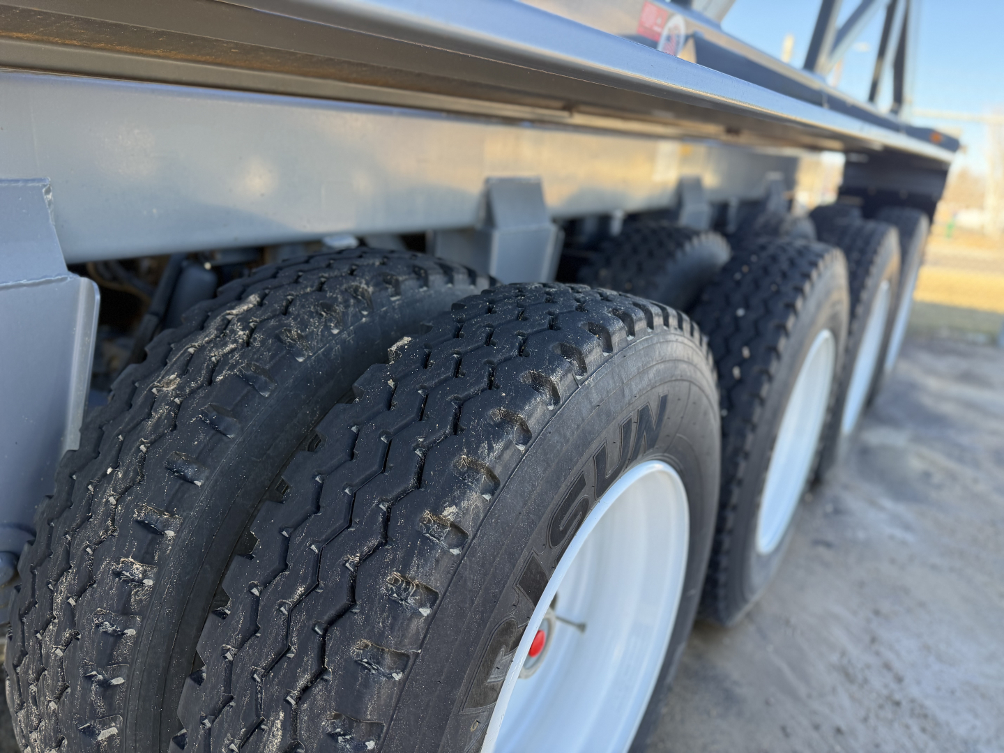 Trailer axles and dual tires on a dump trailer side view. Visible tire brand 'KUMHO' on tread. Aluminum side rails and undercarriage.