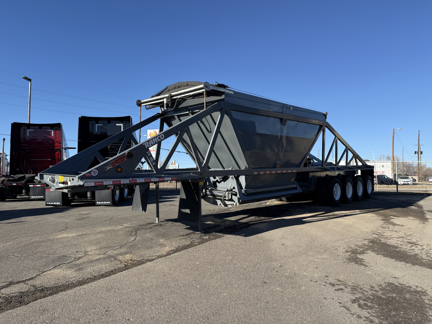 Dump trailer with a long triangular frame and large hopper, LW24464, visible on side with company logo Ranco, triple-axle trailer, black/gray color.