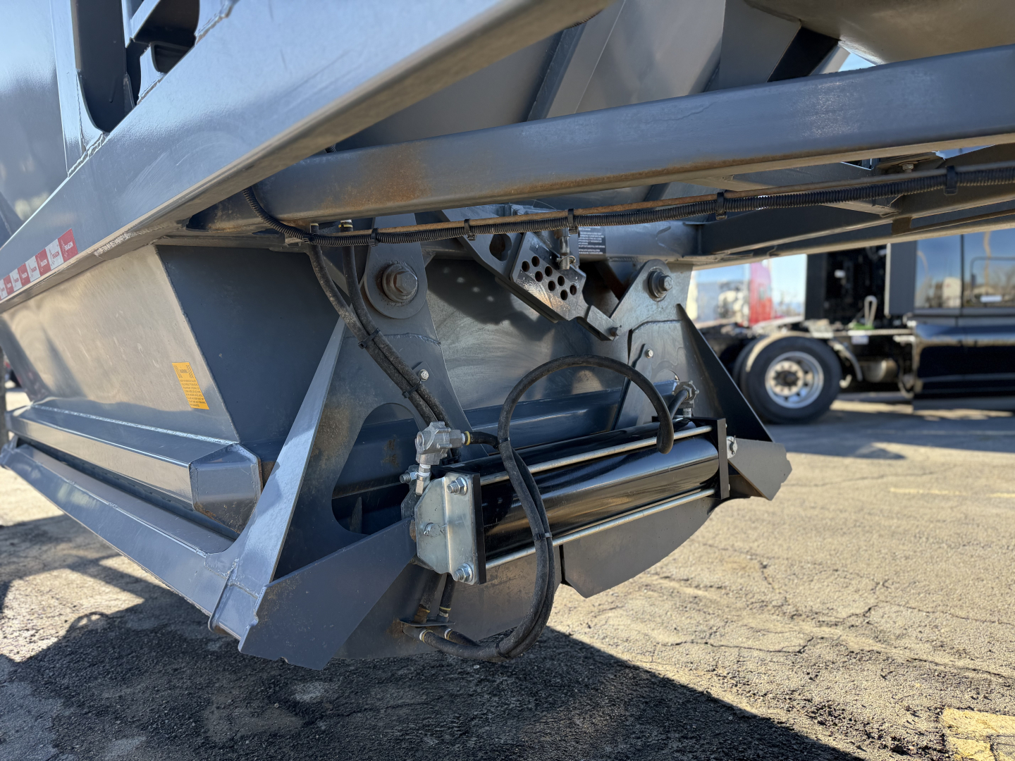 Dump trailer side showing hydraulic hose assembly and undercarriage with winch and frame components, part of Ranco LW24464 trailer model.