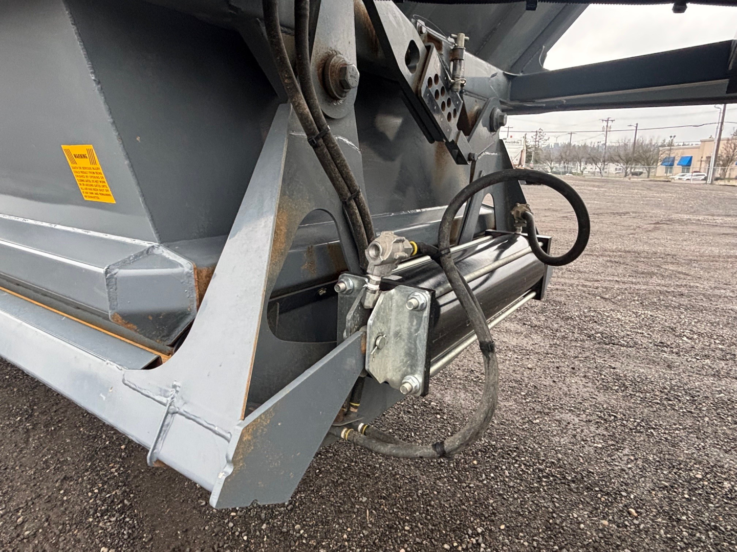 Trailer hitch and hydraulic line assembly on a dump trailer frame showing metal brackets and cables.