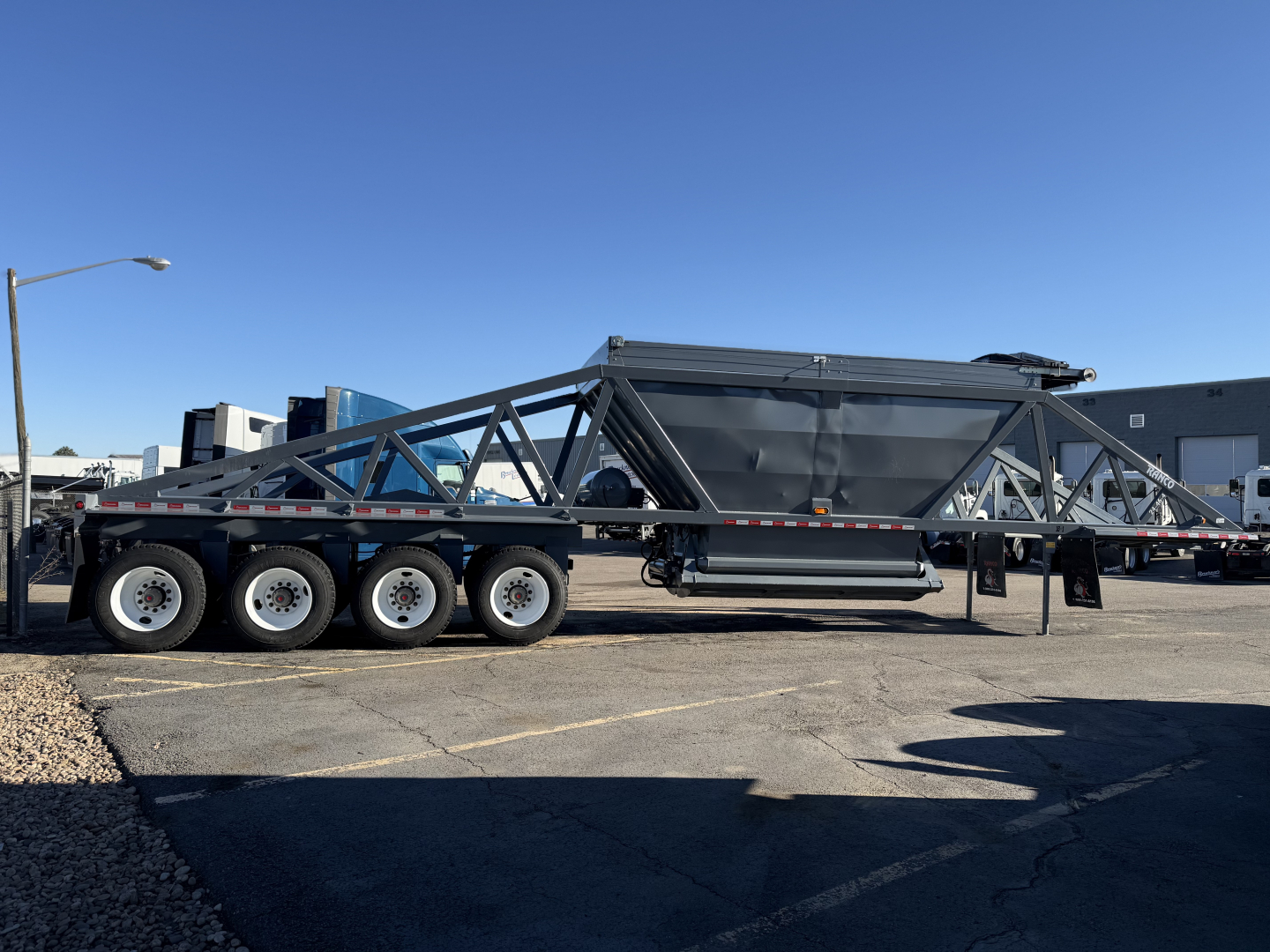 Trailer chassis with multiple axles, metal frame, and a large central hopper using a truss structure; no legible labels visible on the trailer itself.