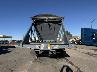 Dump trailer in view showing LW24464 model with hopper and frame structure, front view with metal supports and warning labels, blue semi-trailer in background.