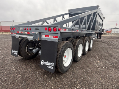 Dump trailer showing GT444A on rear side, multiple wheels, Bruckners dealer mudflaps, and a gray steel frame with a dump bed raised.