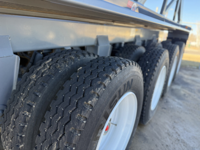 Trailer axles and dual tires on a dump trailer side view. Visible tire brand 'KUMHO' on tread. Aluminum side rails and undercarriage.