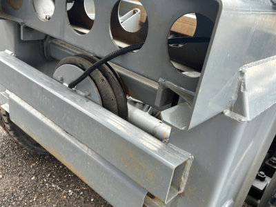 Trailer side frame with wheel hub and rectangular steel crossmember showing hydraulic line and perforated guard, metallic gray surface, no visible branding.