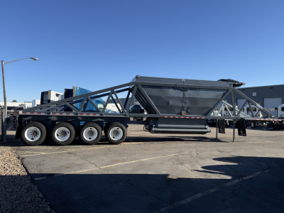 Trailer chassis with multiple axles, metal frame, and a large central hopper using a truss structure; no legible labels visible on the trailer itself.