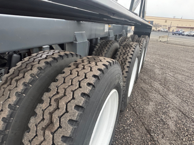 Trailer undercarriage with dual rear axles and large off-road tires; steel frame and suspension components visible.