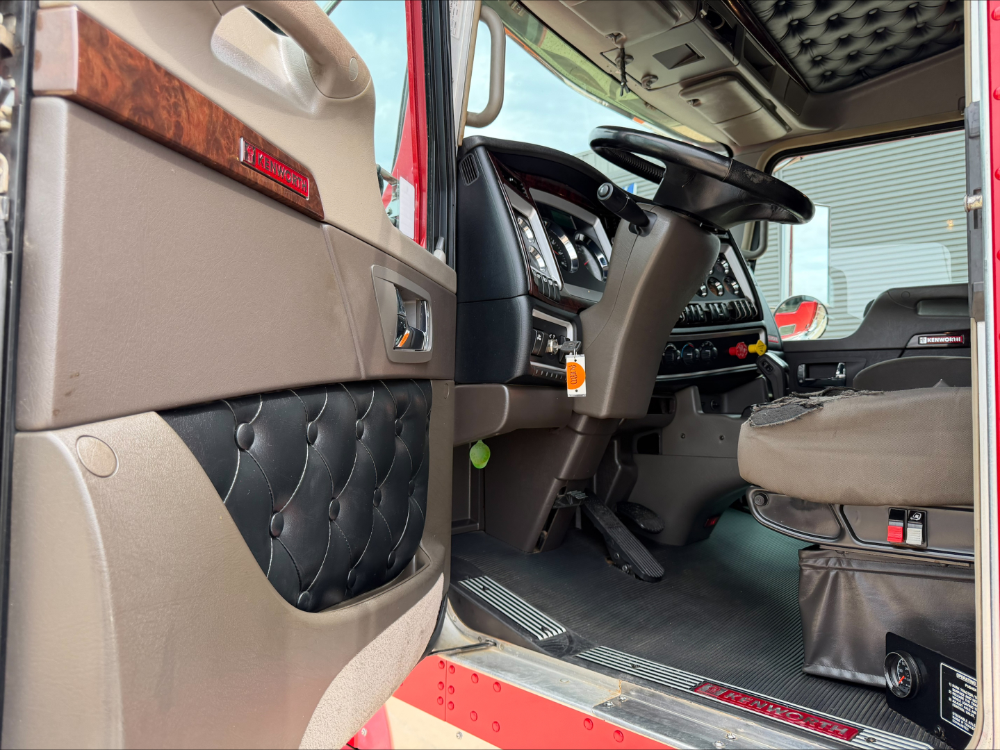 Kenworth W900L truck cab interior showing dashboard, steering wheel, and door panel with leather tufted armrest.