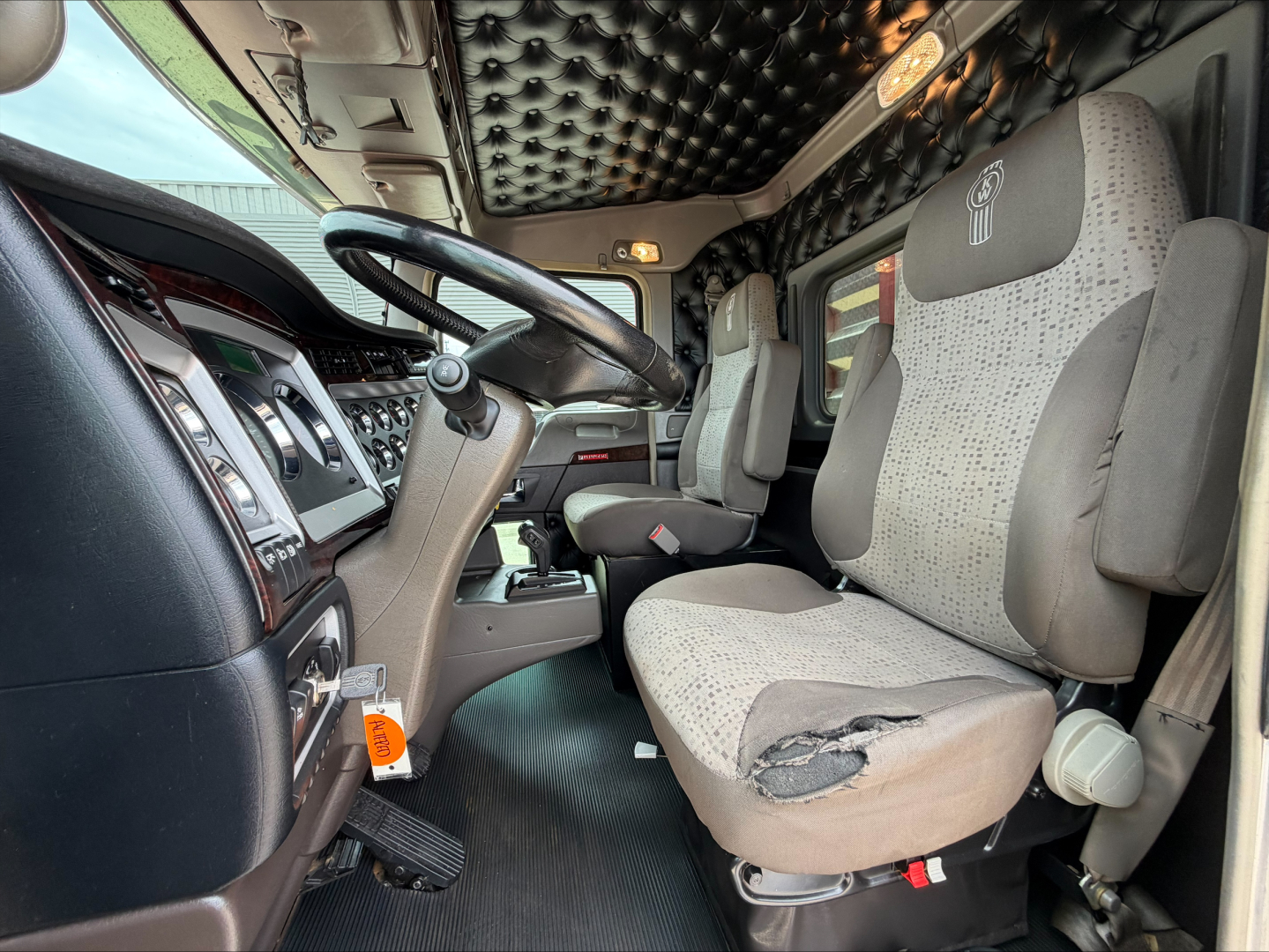 Kenworth W900L truck interior showing steering wheel, dashboard, and torn driver's seat with patterned fabric.