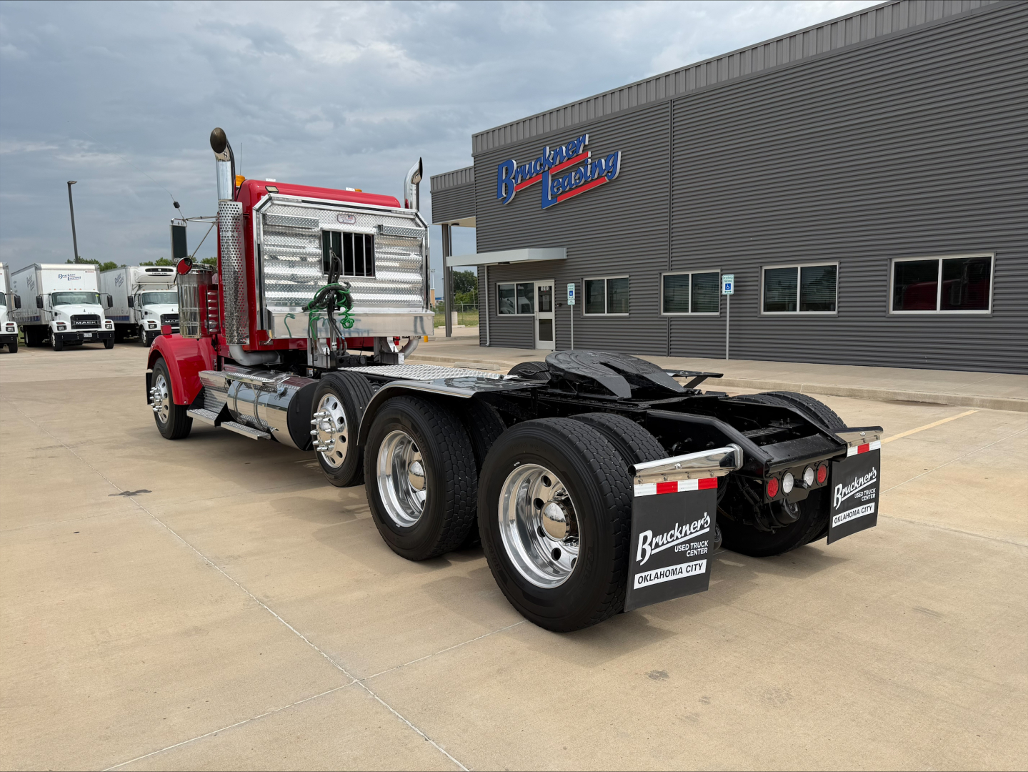 Kenworth W900L tractor with red cab and chrome detailing, rear triple-axle chassis, side view showing fifth wheel and dual rear wheels.