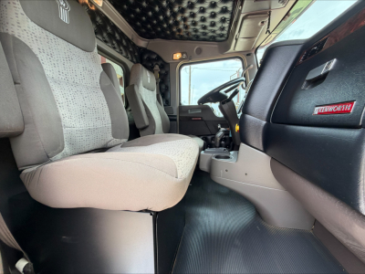 Kenworth W900L truck cab interior showing front seats, steering wheel, dashboard, and craftsmanship with quilted headliner.