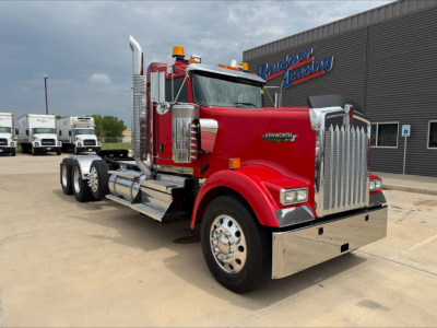 Kenworth W900L conventional daycab truck in red with chrome grille and dual stacks, front-left angle view, outdoor dealership lot.
