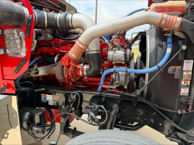Kenworth W900L engine bay showing red engine block, large intake tubing, aluminum intercooler piping, blue hose, and various warning labels.