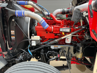 Kenworth W900L truck engine bay showing bright red engine with X15 badge, blue silicon hoses, radiator, coolant reservoir, and various connectors.