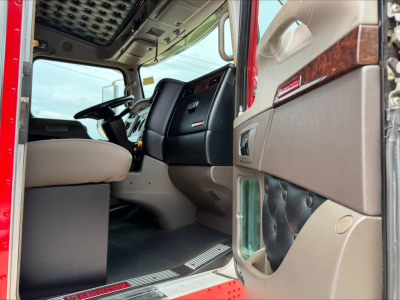 Interior of Kenworth W900L truck cab viewed from doorway showing steering wheel, dashboard, and beige door panel with wood trim