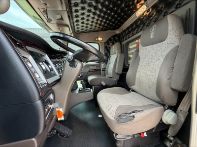 Kenworth W900L truck interior showing steering wheel, dashboard, and torn driver's seat with patterned fabric.