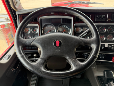 Steering wheel and instrument cluster of a Kenworth W900L truck cab, showing gauges and dashboard controls.