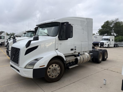 Truck cab side view showing Volvo VNR series sleeper tractor with white exterior and dual rear axles.
