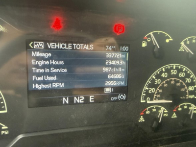 Vehicle totals screen in a Volvo VNR showing mileage 33772 miles, engine hours 23409.3h, time in service 987?h, fuel used 64686 G, highest RPM 2956, gear N N2 E, temp 74°F, speedo gauges visible.