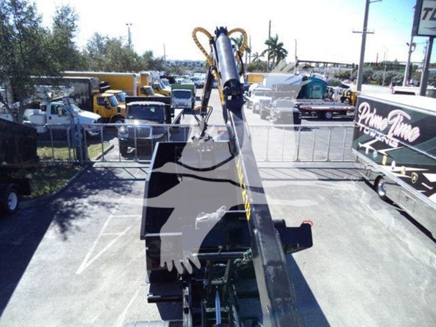 Peterbilt 337 roll-off truck crane arm extending from flatbed with surrounding yard of heavy equipment.