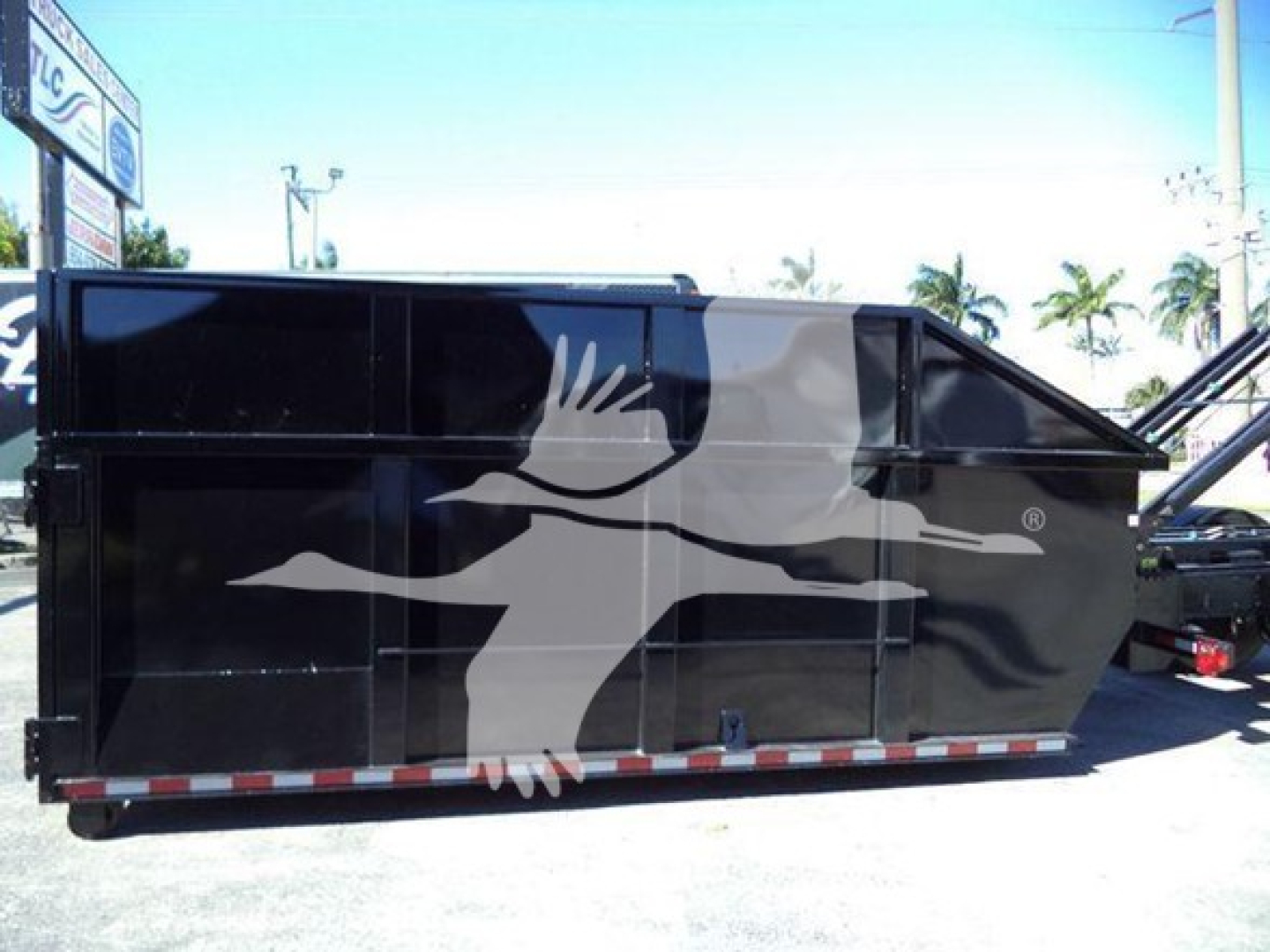 Peterbilt 337 roll-off truck with large black waste container, side view.