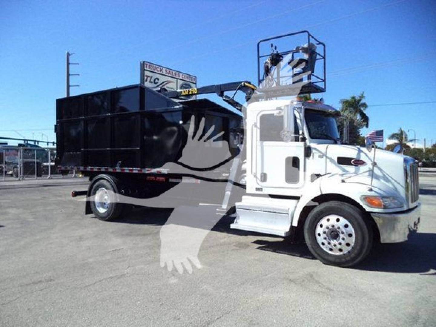 Peterbilt 337 roll-off truck in a lot, white cab with black dump body, side mirrors, ladder 'cherry picker' crane on top, no visible branding text legible.