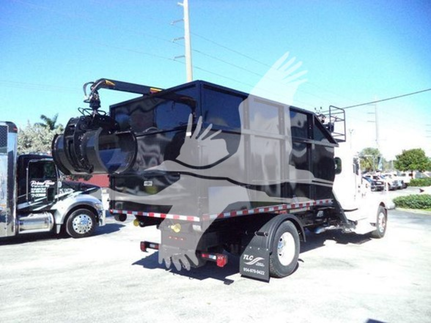 Peterbilt 337 roll-off truck in a lot, rear and side views visible, black dump body. Visible labels include stock and contact area letters on side of cab and rear.