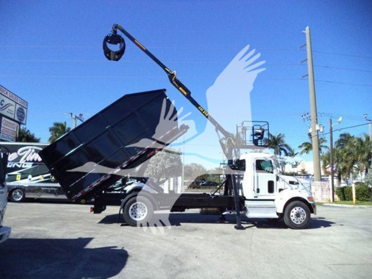 Peterbilt 337 roll-off truck with hydraulic dump bed and crane in raised position; side shows no legible text due to watermark.