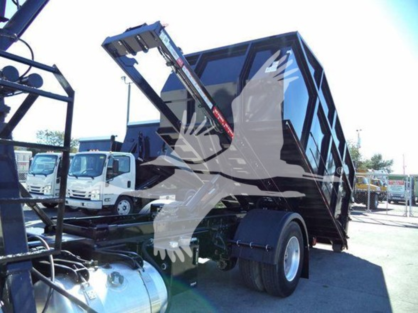 Peterbilt 337 roll-off truck with raised dump bed and hydraulic hoist in a dealer lot.