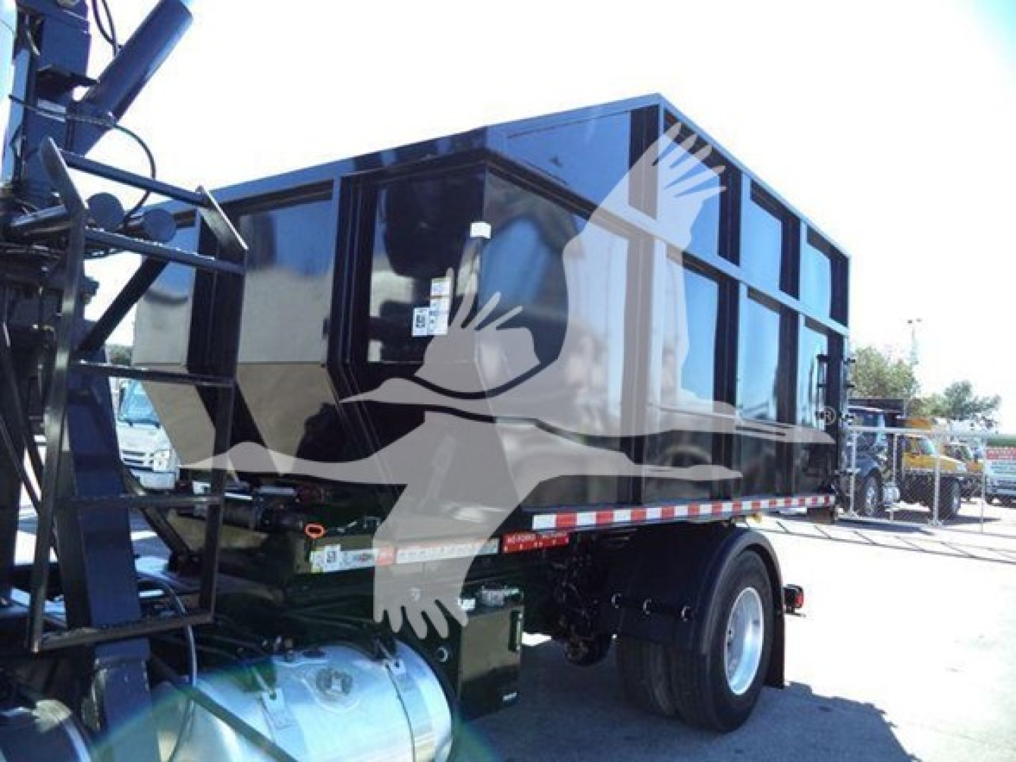 Peterbilt 337 roll-off truck rear quarter with black dump body, dual rear wheels, and hydraulic lift mechanism visible.