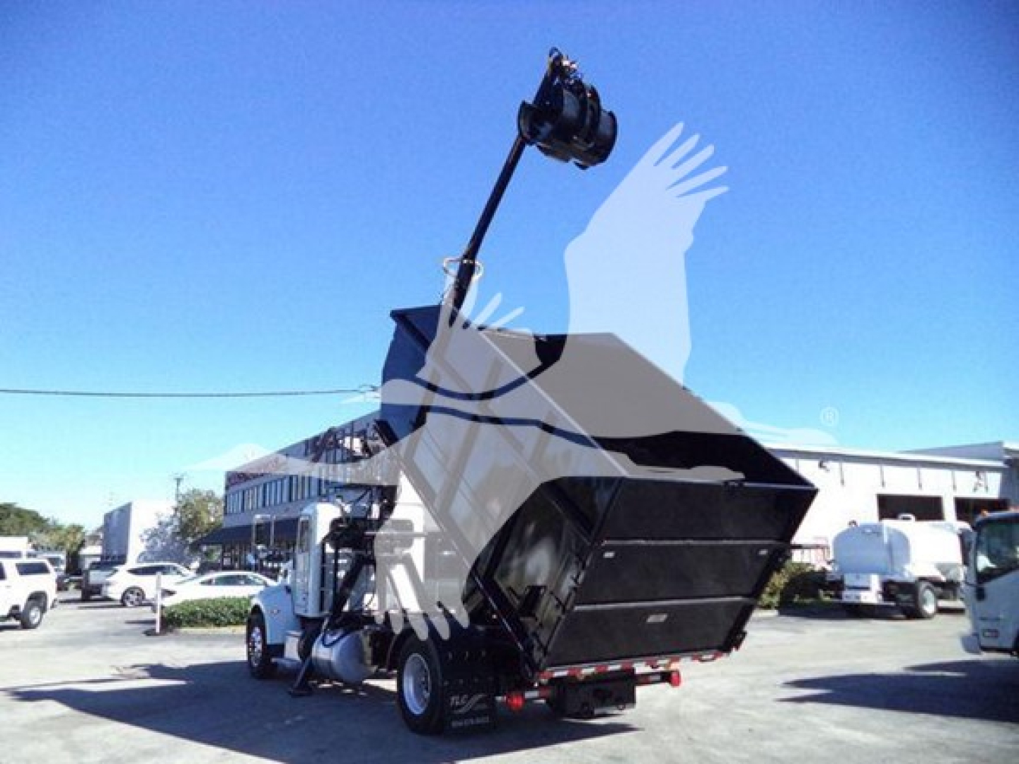 Peterbilt 337 rolloff truck rear view with tipped bed and crane in yard showing concrete loading area.