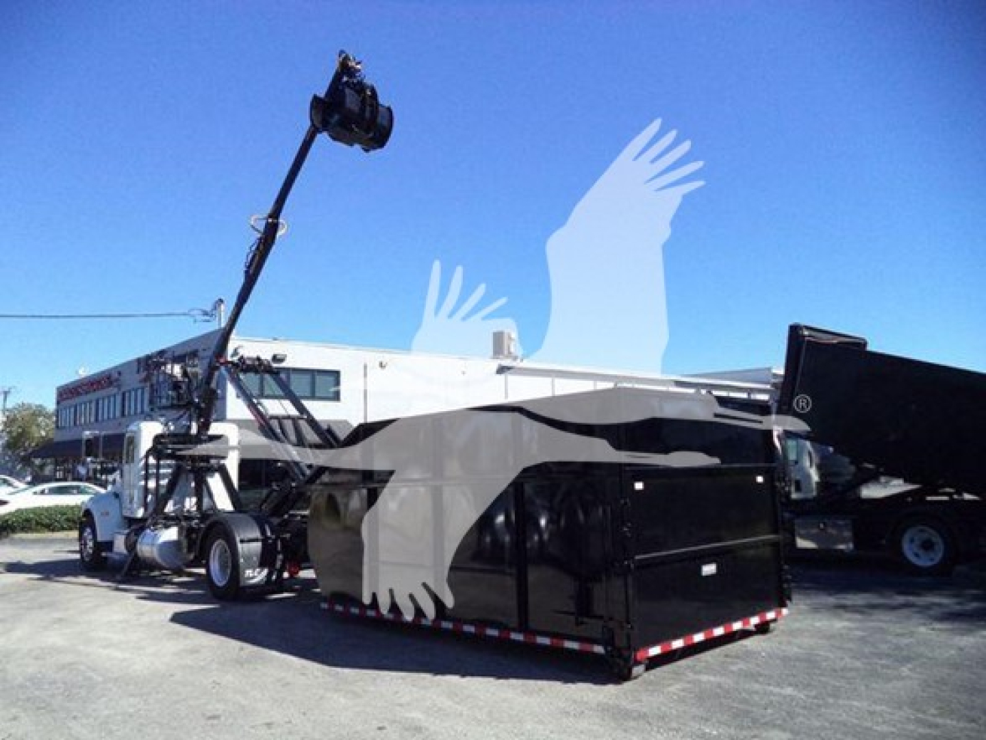 Peterbilt 337 roll-off truck with crane in front, black roll-off container, white cab, blue sky.