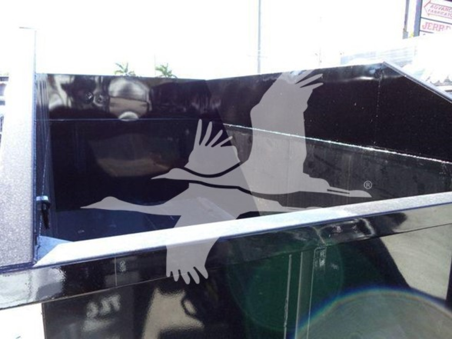 Truck bed side with graphic of two white birds in flight and reflection, part of Peterbilt 337 roll-off truck; no legible serials or labels visible.