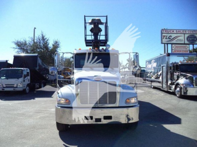 Front view of a white 2020 Peterbilt 337 roll-off truck with a raised platform crane on the cab roof, chrome grille, and nearby trucks in a dealership lot.