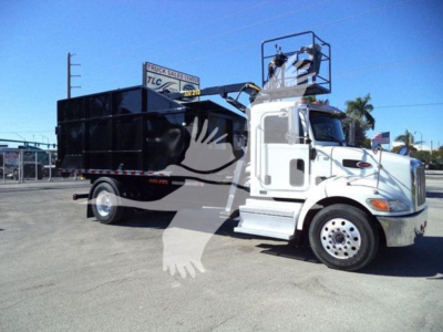 Peterbilt 337 roll-off truck in a lot, white cab with black dump body, side mirrors, ladder 'cherry picker' crane on top, no visible branding text legible.
