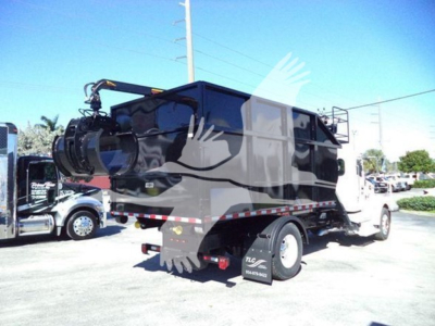 Peterbilt 337 roll-off truck in a lot, rear and side views visible, black dump body. Visible labels include stock and contact area letters on side of cab and rear.