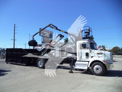 Peterbilt 337 roll-off truck in service showing hydraulic arm and large black dumpster bed with white cab and crane.